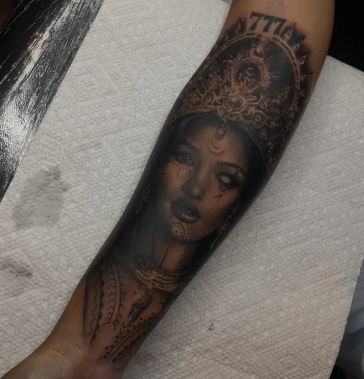 Black-and-grey forearm portrait with ornate headdress.