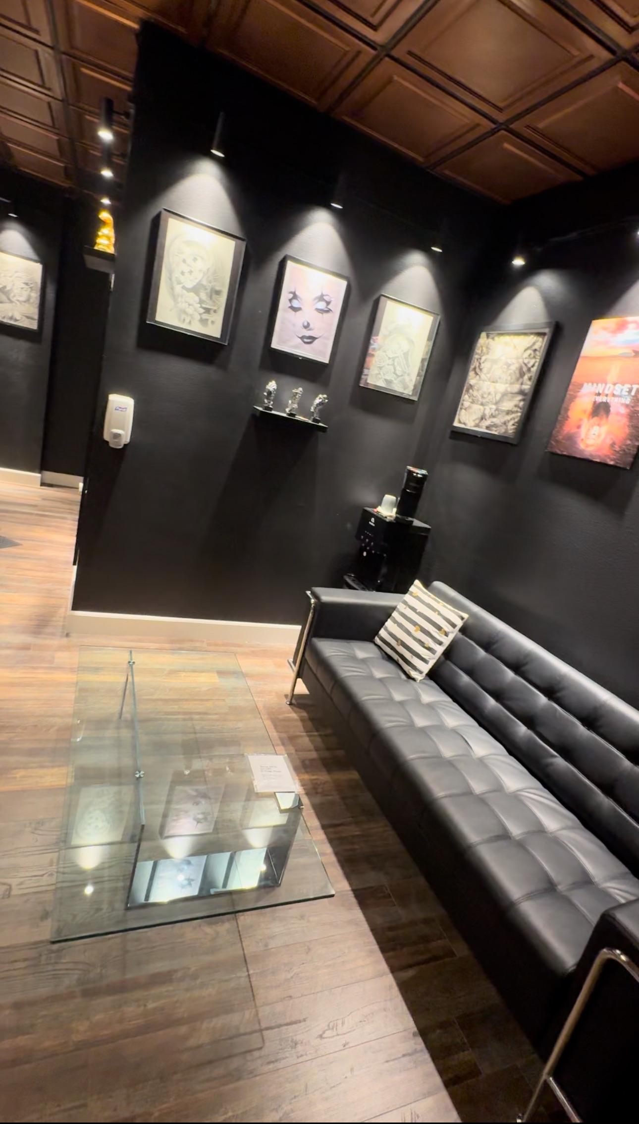 Tattoo Nerds client lounge with a leather couch, glass table, and framed artwork